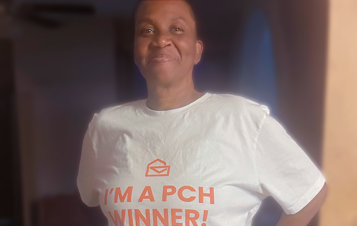 A person smiles while wearing a white t-shirt that says, 'I'm a PCH Winner!'