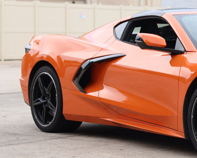 A close-up view of the side and rear of a modern orange sports car with black accents.