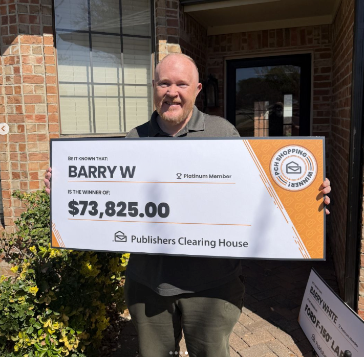 A smiling man holds a large Publishers Clearing House check for $73,825.00 outside a brick house.