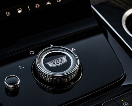A close-up of a silver rotary dial with the Cadillac logo on a black vehicle center console.