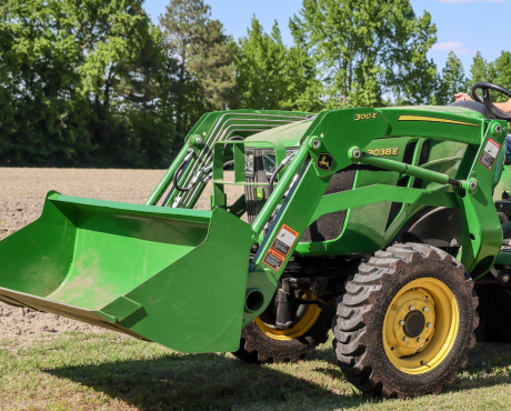 A green John Deere 3038E tractor with a front loader is parked on grass next to a field.