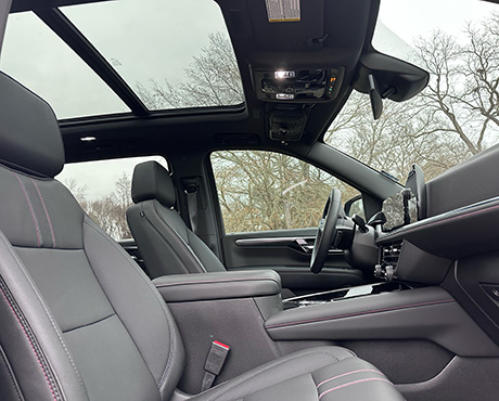 The interior of a vehicle showing the front seats, dashboard, and a large sunroof.
