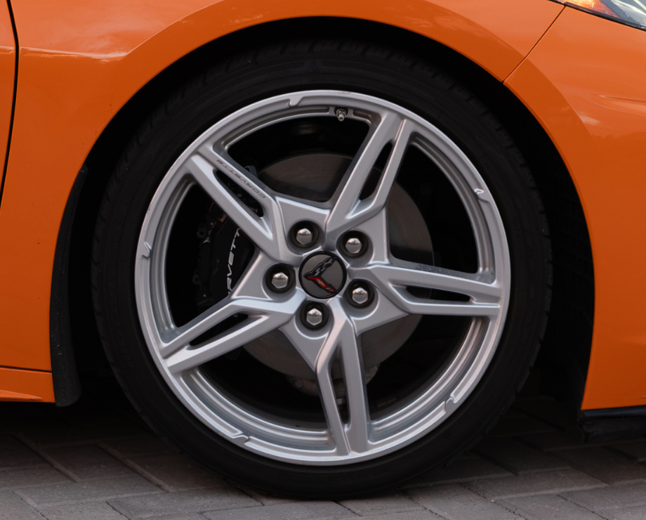The back of an orange convertible Corvette with its tail lights on, parked on a cobblestone driveway.