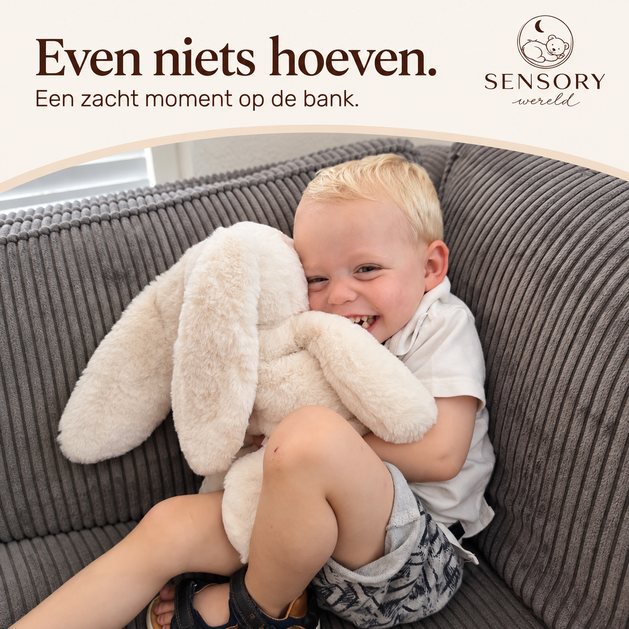 Kind in een witte polo dat het konijn omarmt op een grijze bank.