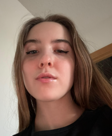 A close-up, low-angle photo of a young woman with long, light brown hair and winged eyeliner.