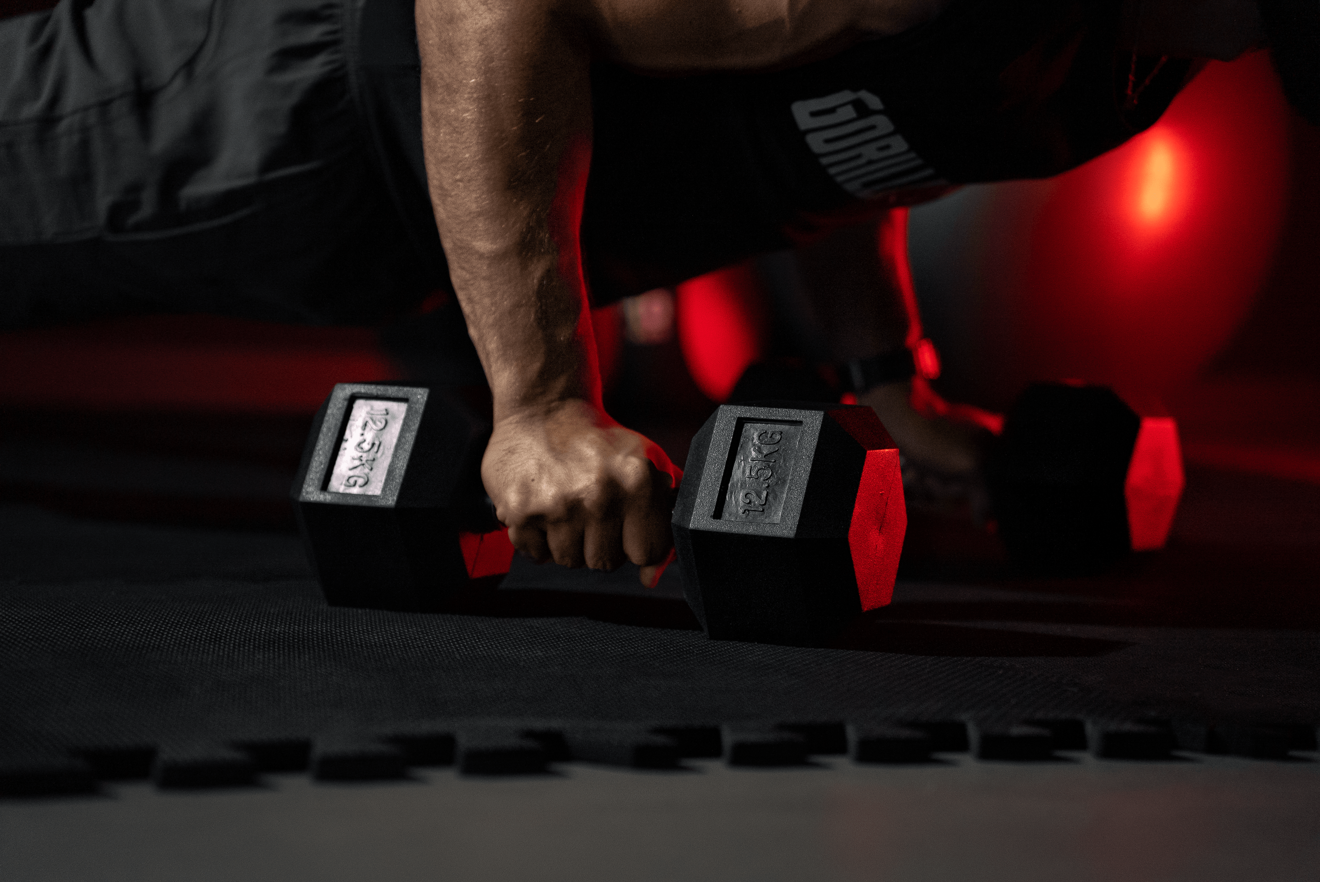 Person doing push-ups with dumbbells on a gym mat, lit by red light.
