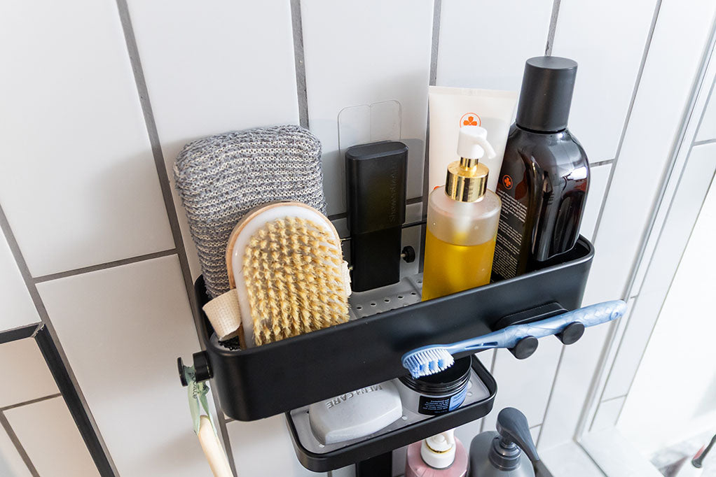 A black shower caddy filled with various toiletries and attached to a white tiled wall.
