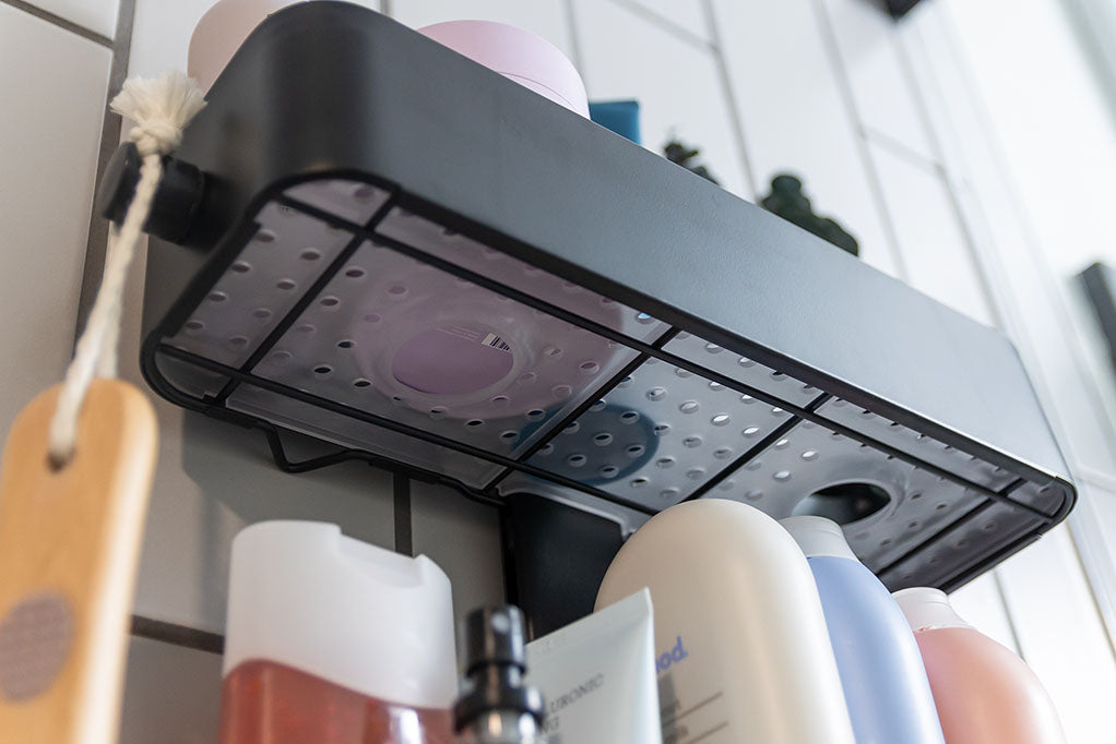 A low-angle view of a black shower caddy mounted on a white tiled wall, filled with toiletries.