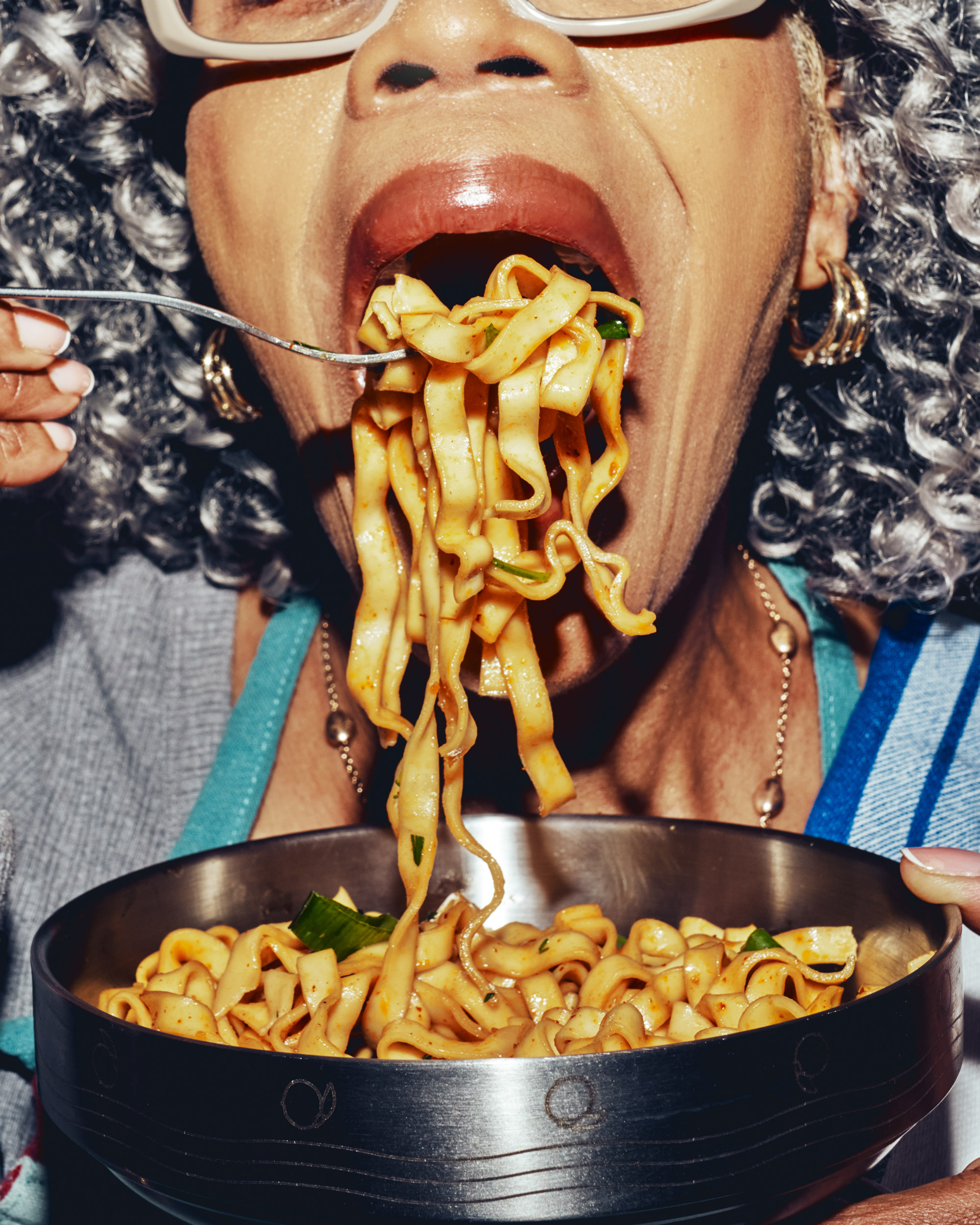 Person eating noodles from a metal bowl with a fork.