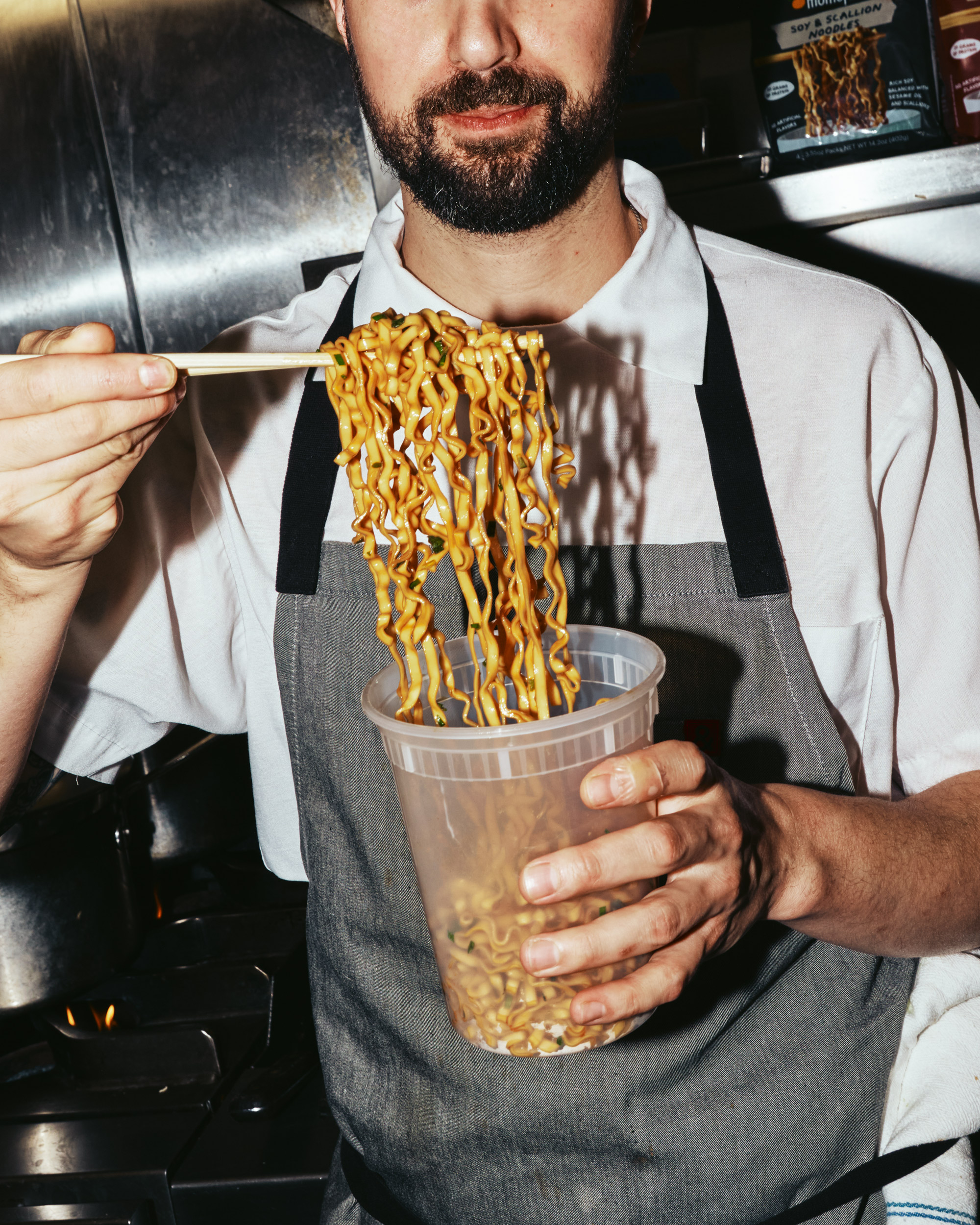 Person holding chopsticks with noodles over a plastic container.