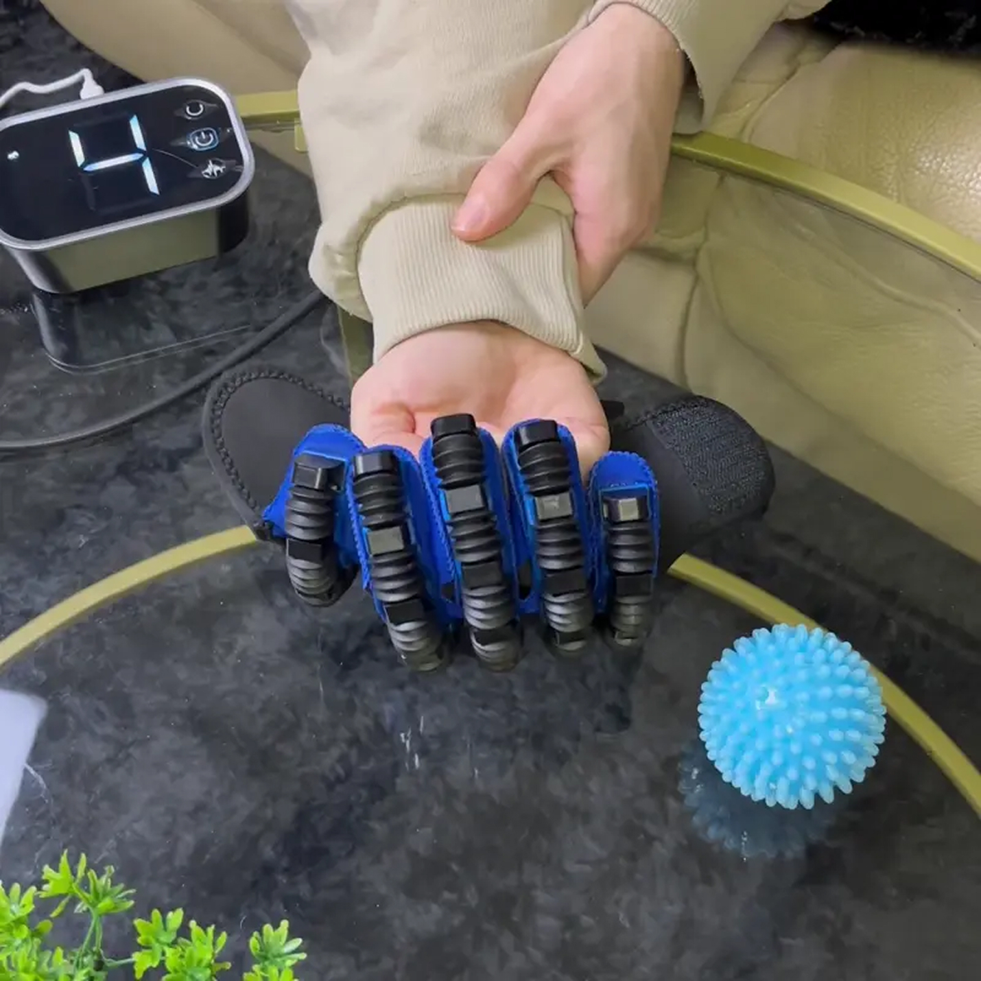 A hand wearing a robotic glove next to a spiky blue ball on a table.