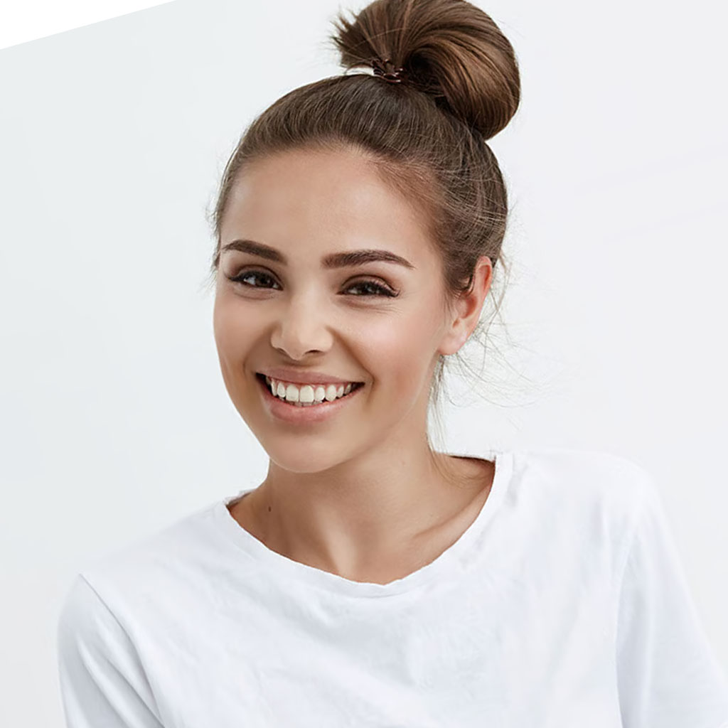 Smiling person with hair in a bun, wearing a white shirt.