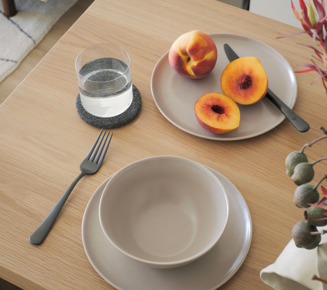 Peach slices and whole peach on a plate, glass of water, fork, and bowls on a wooden table.