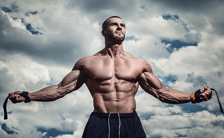 Muscular man exercising with resistance bands under a cloudy sky.