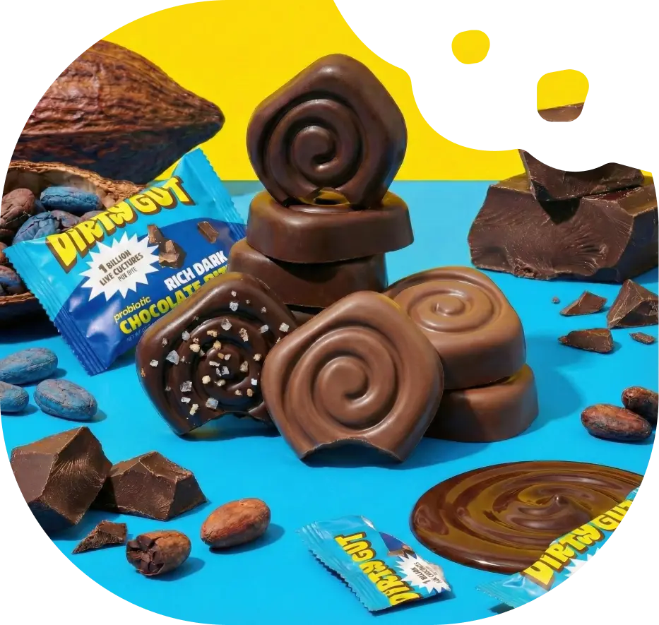 An arrangement of Dirty Gut probiotic chocolate bites, cacao beans, and chunks of chocolate on a colorful background.