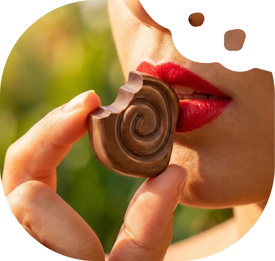 A close-up of a person with red lipstick taking a bite out of a spiral-shaped piece of chocolate.