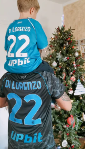 Two people in matching jerseys stand by a decorated Christmas tree.