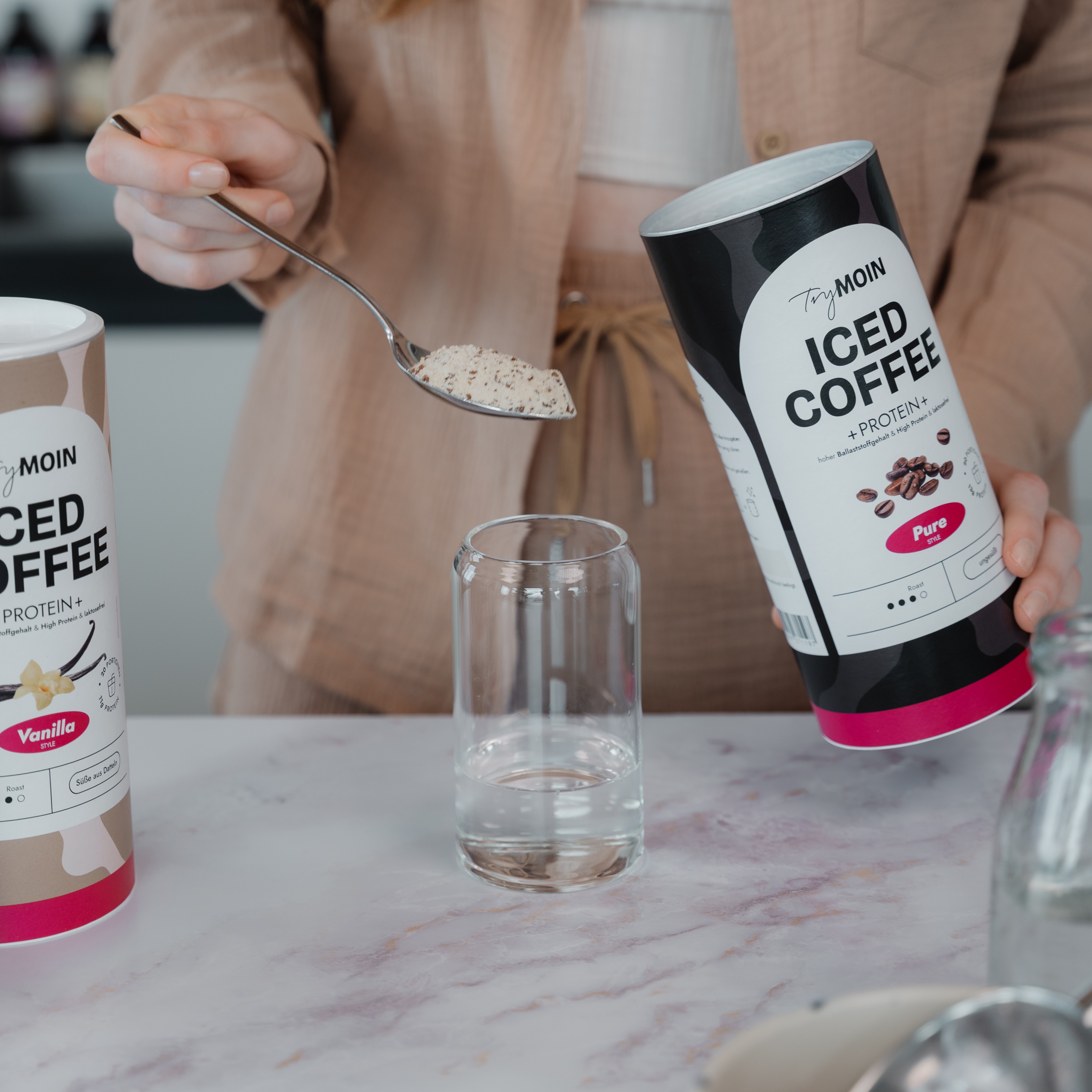 Person scooping iced coffee powder into a glass from a container.