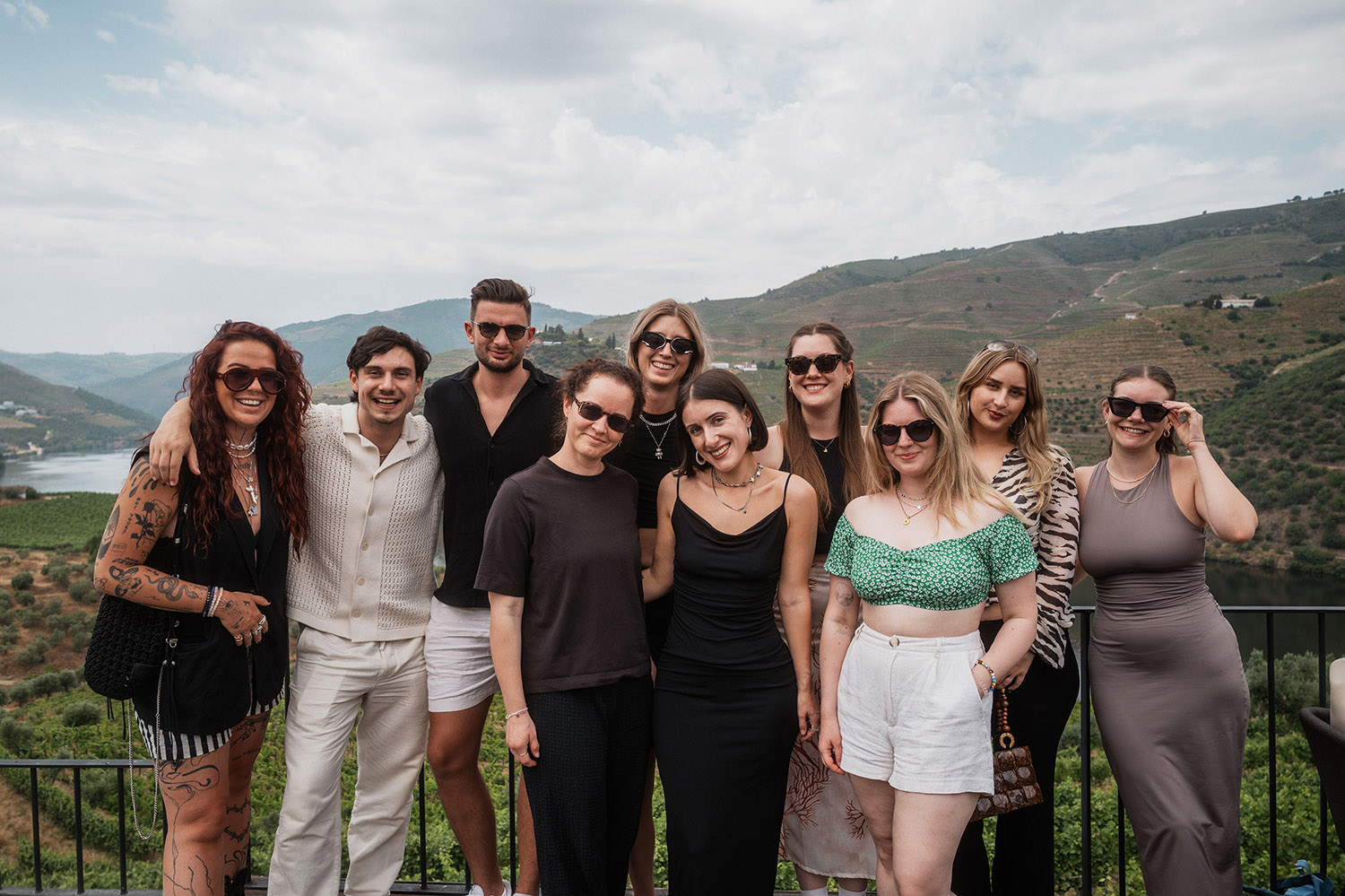 A group of ten people posing for a photo on a terrace overlooking a river and terraced hills.