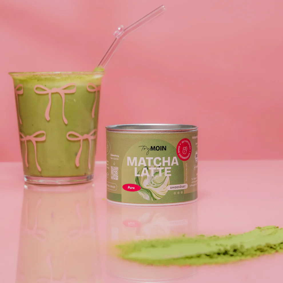 A green matcha latte in a glass with a can of matcha powder.