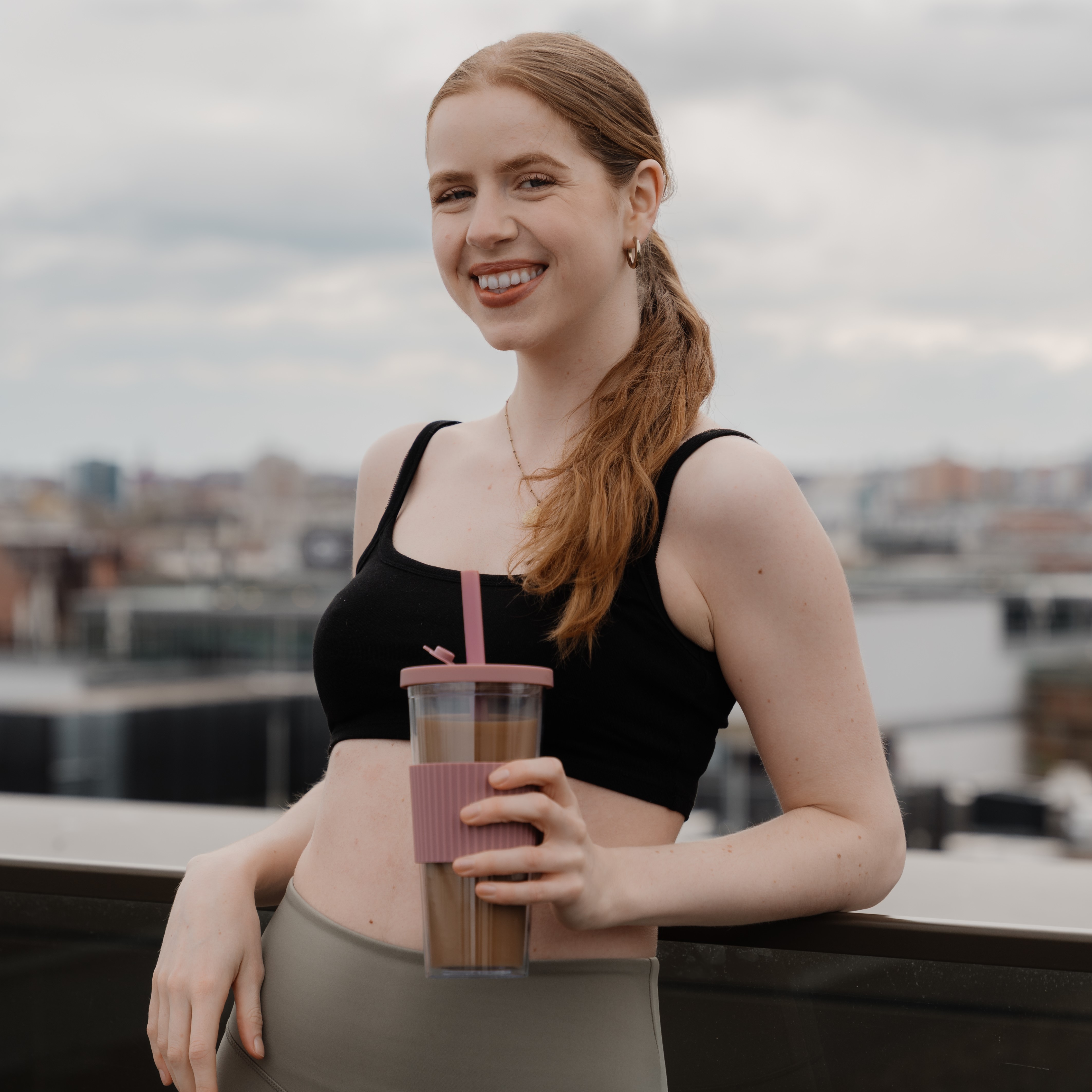 Woman in workout attire holding a tumbler on a rooftop.