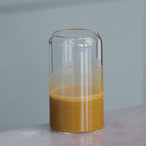 A glass of orange liquid being stirred on a table.