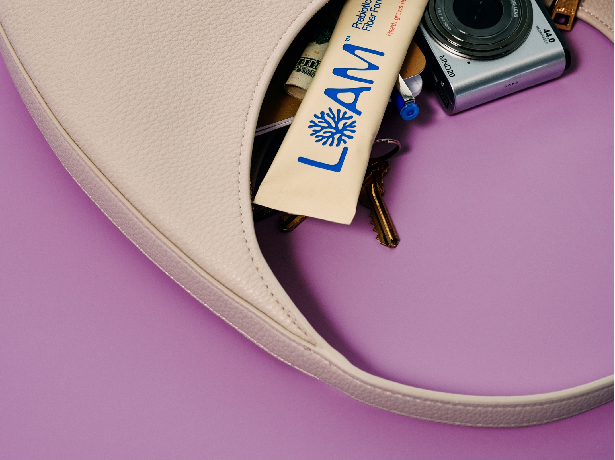 An overhead view of a white handbag on a purple surface, with its contents spilling out.
