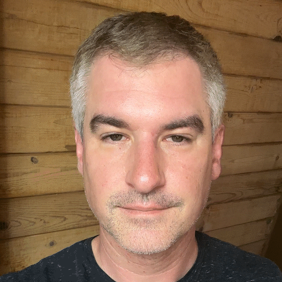 A person with short hair against a wooden wall background.