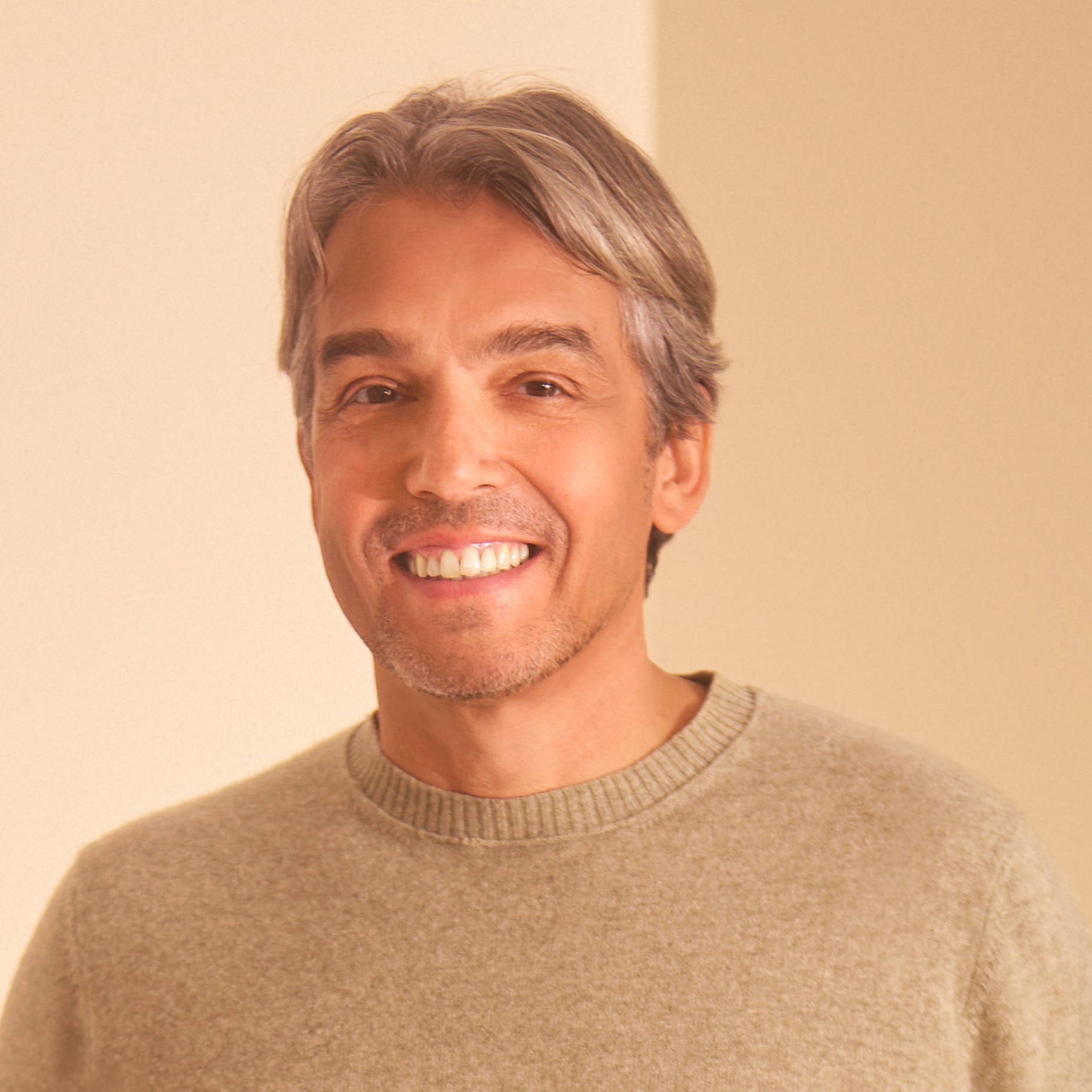 A smiling middle-aged man with graying hair wearing a tan sweater.