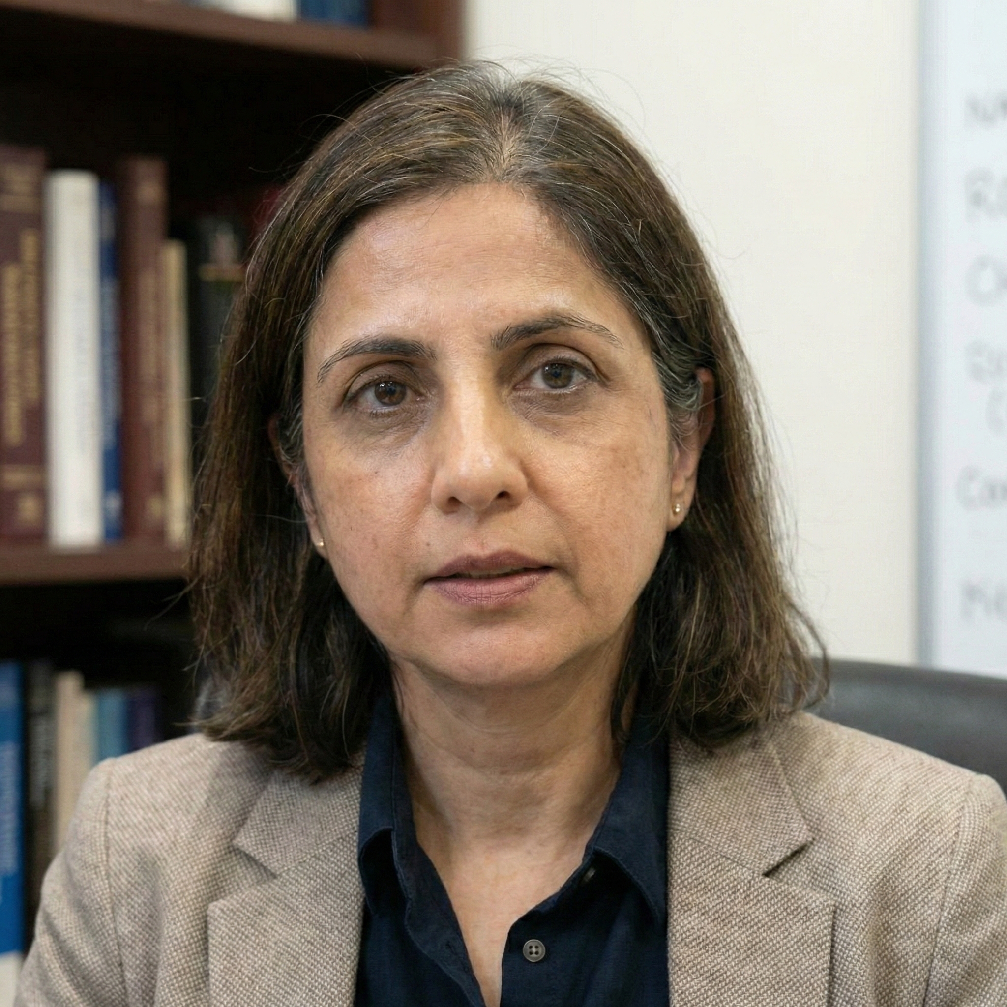 A headshot of a woman with shoulder-length hair in a blazer, posing in front of a bookshelf.