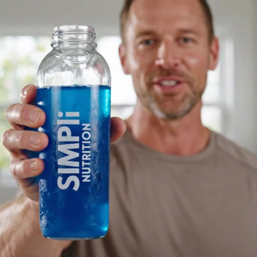 A man holds a bottle of blue Simpli Nutrition liquid towards the camera.