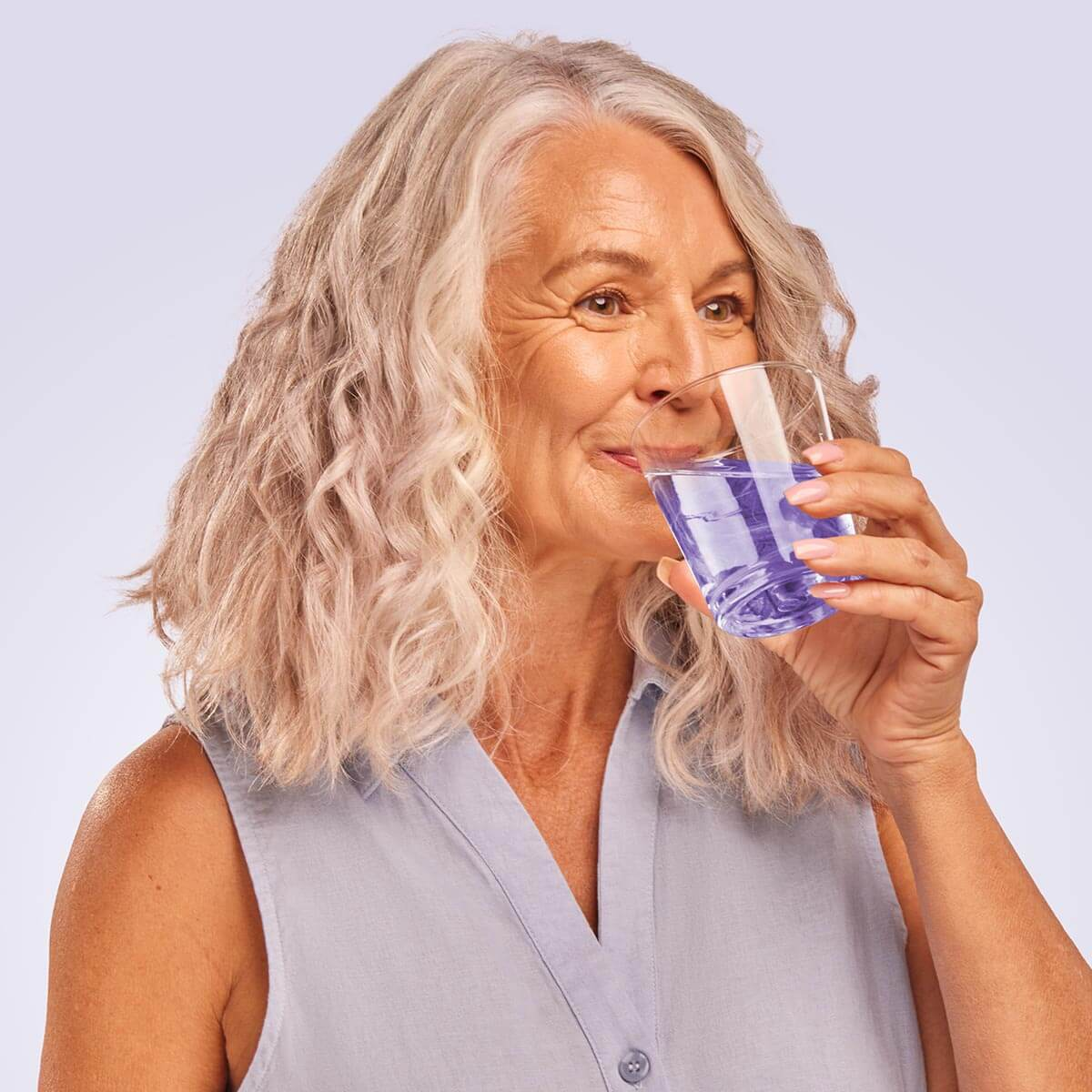 Woman holding a glass with blue liquid, smiling.