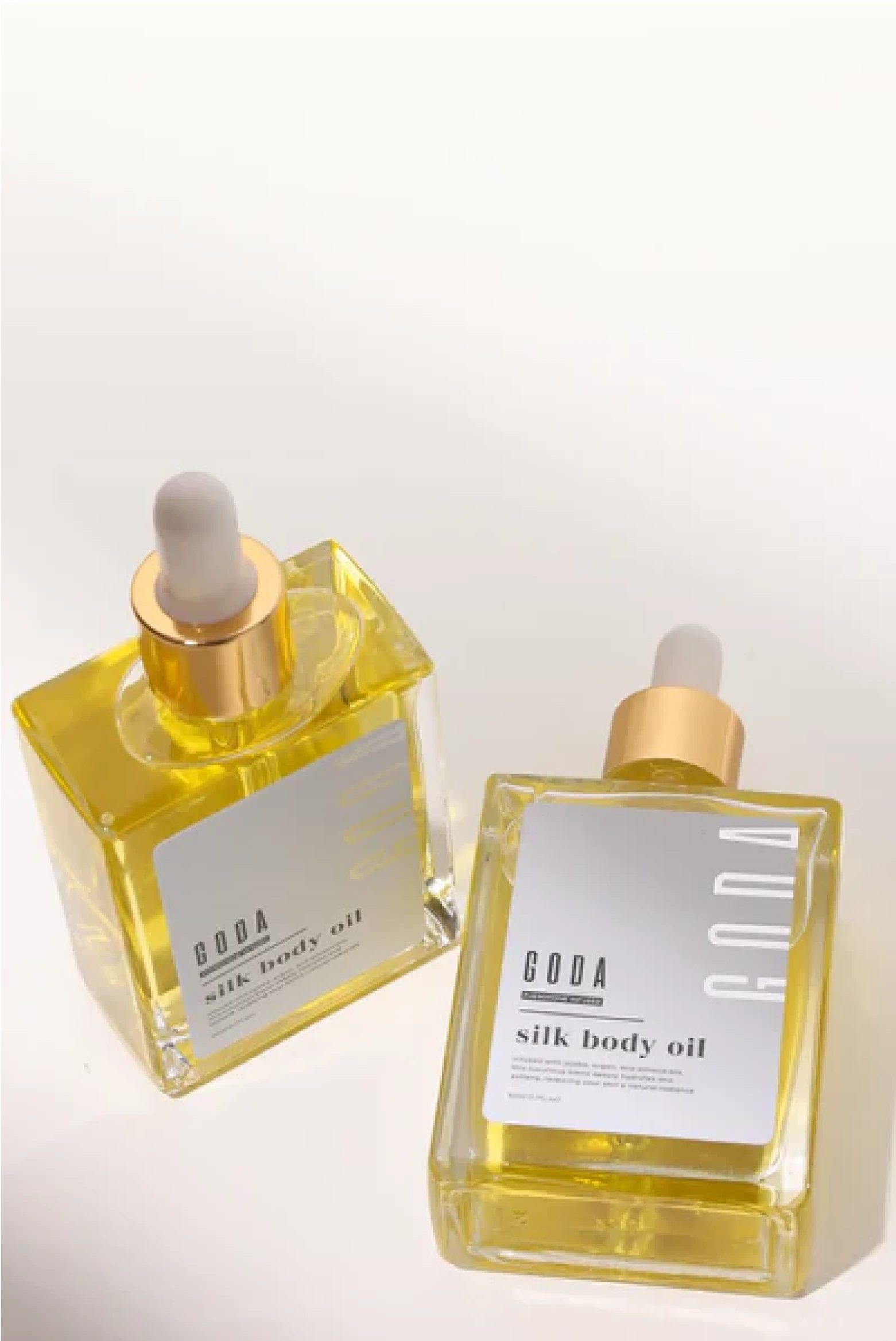 Two square bottles of silk body oil with droppers on a light background.