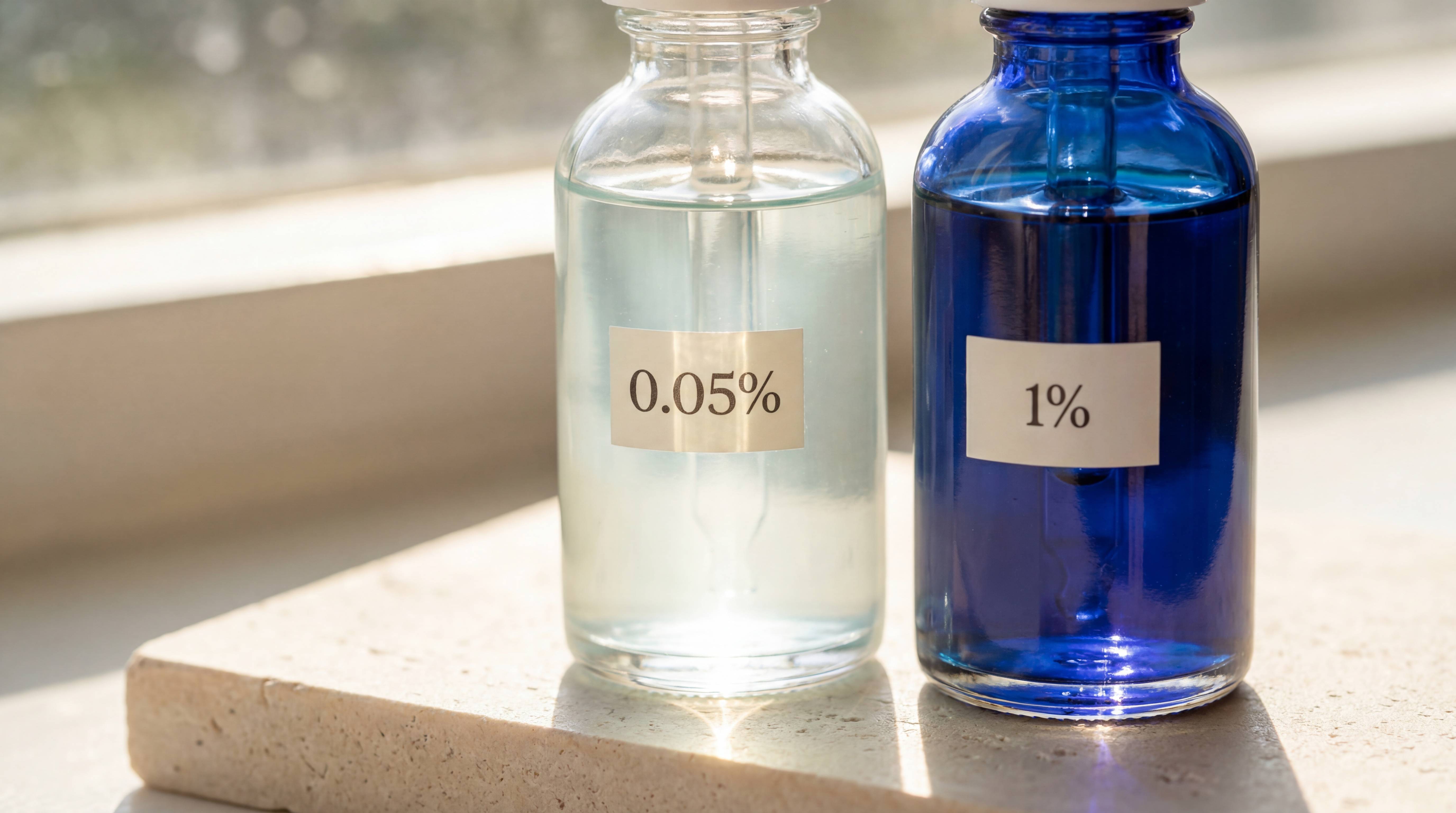 Two glass dropper bottles, one clear labeled 0.05% and one blue labeled 1%, on a stone ledge.