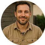Smiling man with a beard in a brown shirt, standing outdoors.
