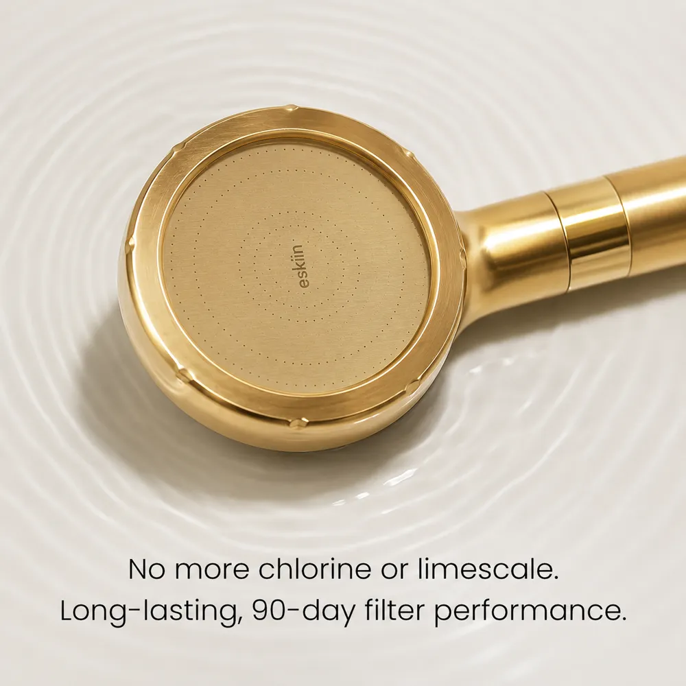 A gold-colored handheld shower head rests on a white surface with water ripples.