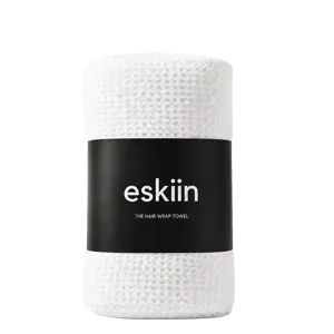 A rolled-up white waffle-weave hair wrap towel with a black label that reads 'eskiin'.