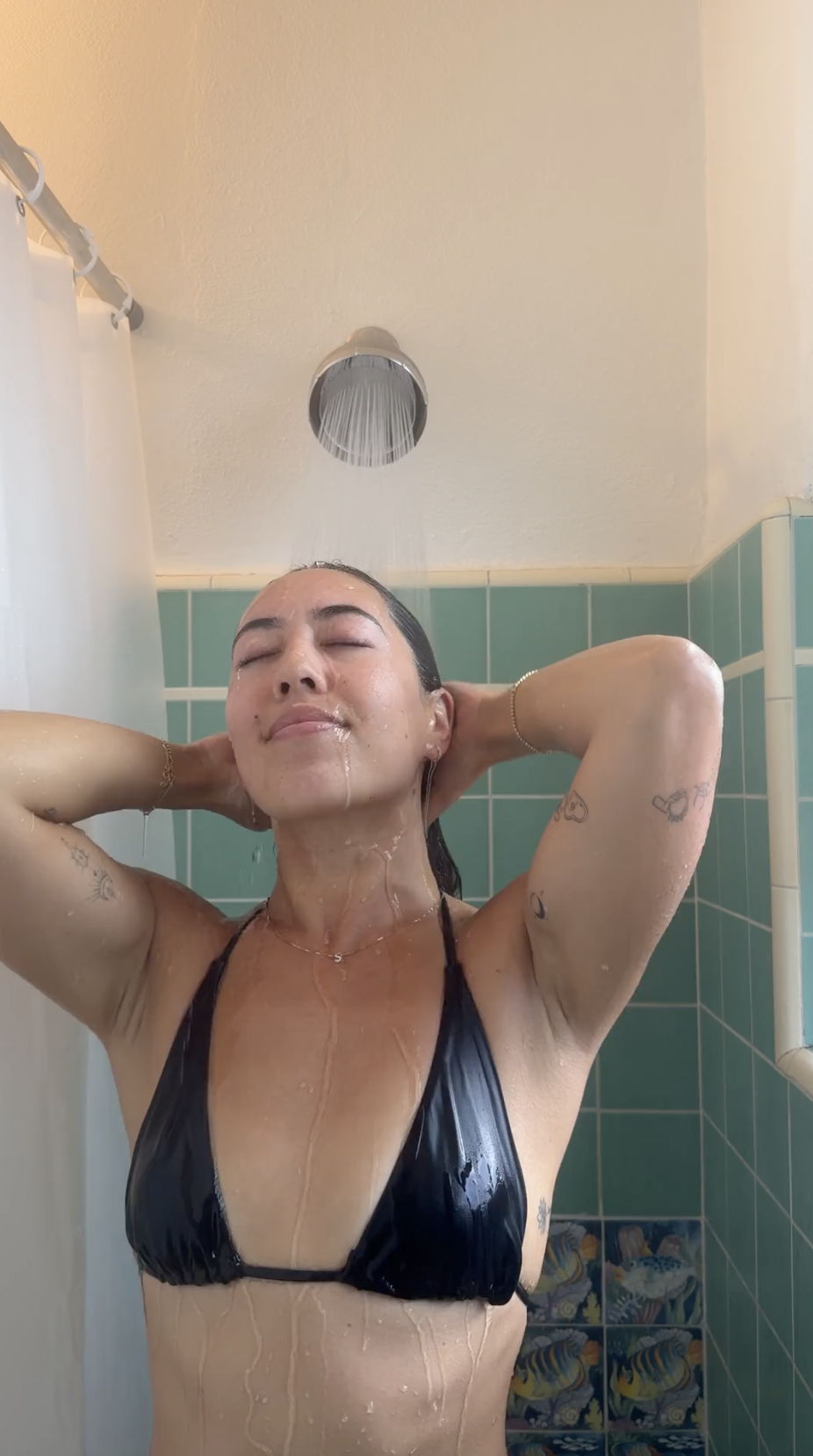 Person showering with water flowing over face and dark tiles in the background.