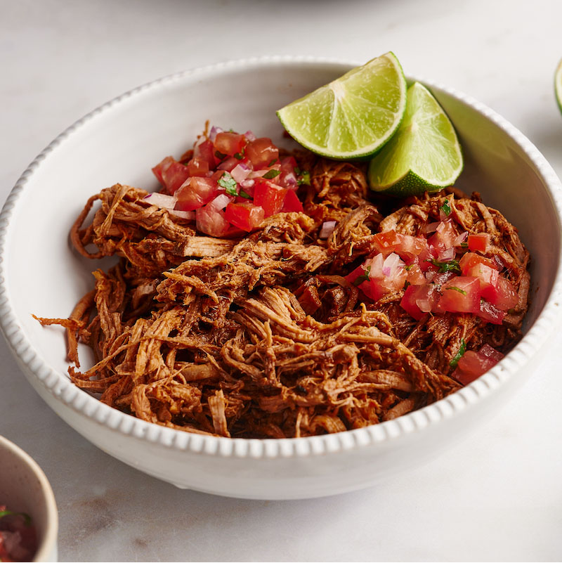 Shredded beef with tomato salsa and lime wedges in a white bowl.