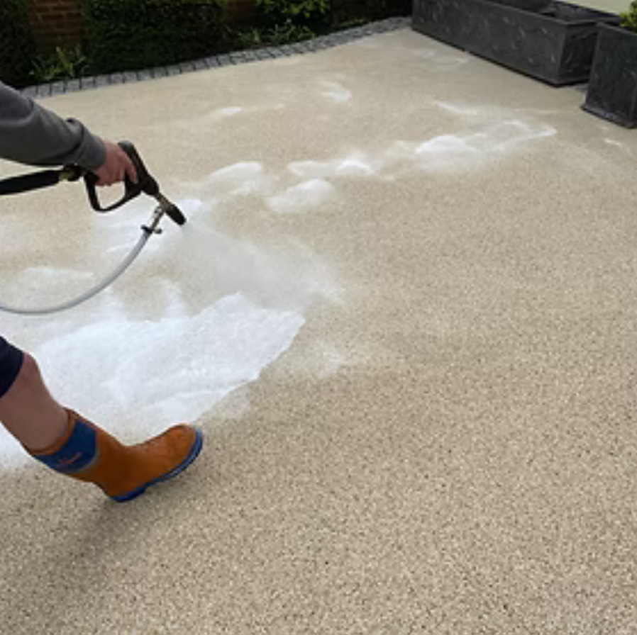 Person spraying foam on a paved surface outdoors.