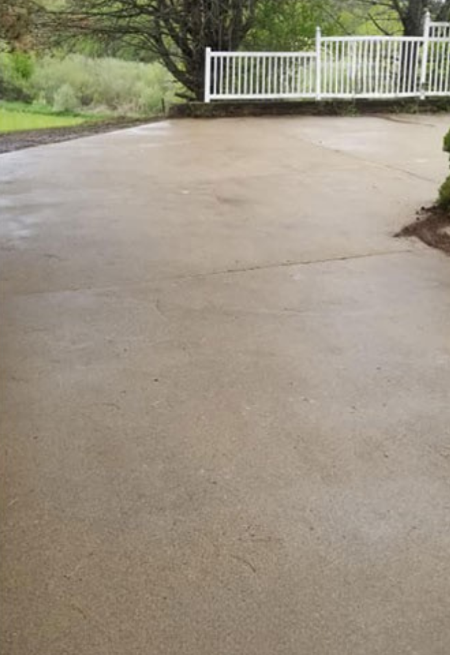 Concrete patio with white fence and trees in the background.