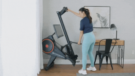 Woman folding a rowing machine in a home office setting.