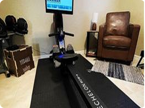 Home gym setup with a rowing machine, weights, and a brown chair.