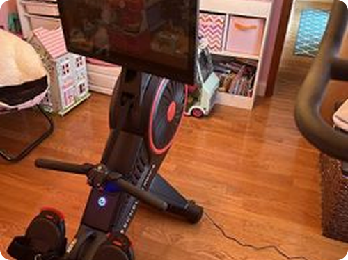 Treadmill in front of a grey couch with cushions in a room with wooden flooring.
