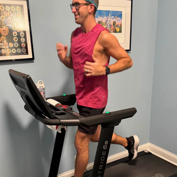 Person running on a treadmill wearing a pink tank top and shorts.