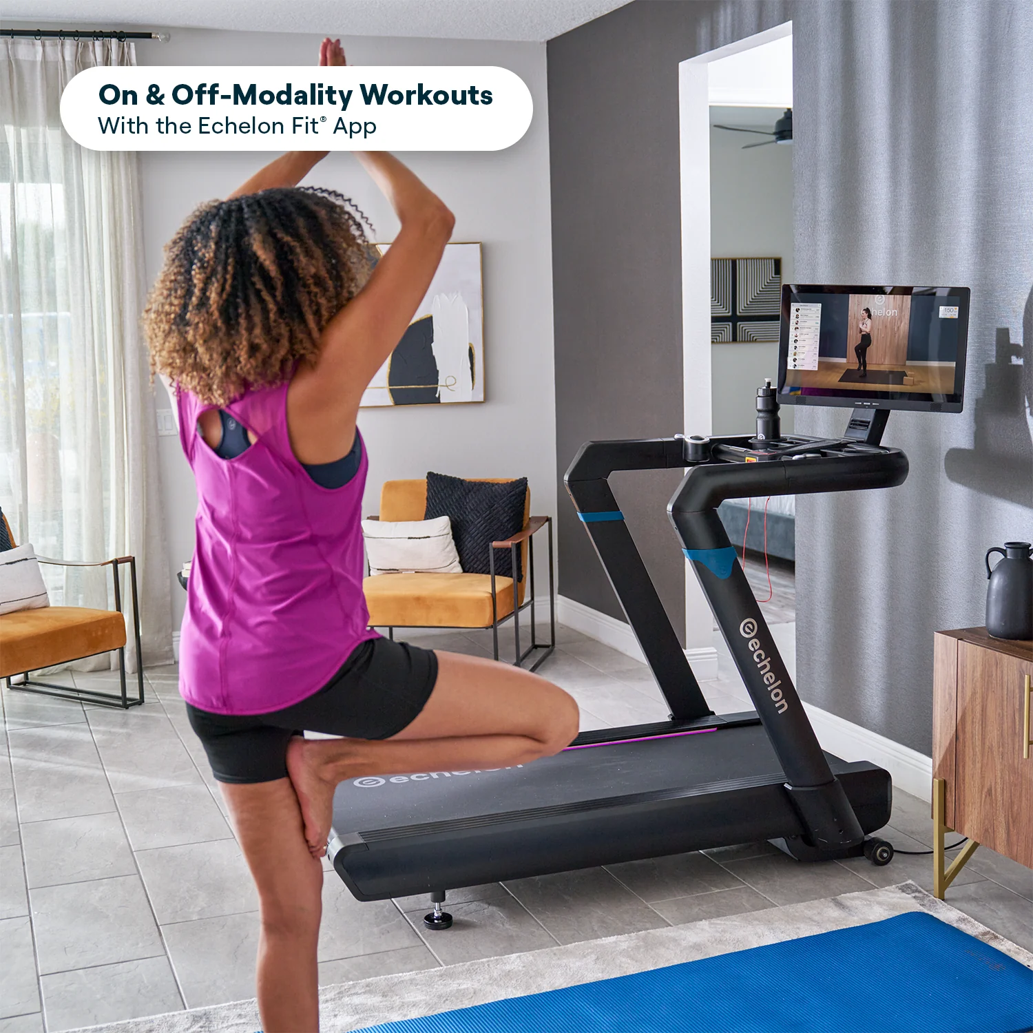 A woman does a yoga pose in a living room next to an Echelon treadmill with a screen.