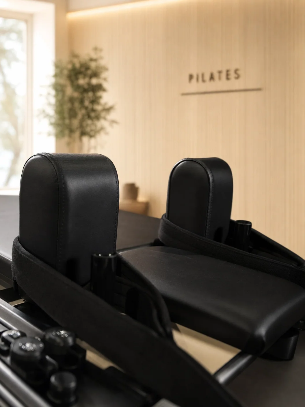 A close-up of a black Pilates reformer machine in a studio with a wood-paneled wall.