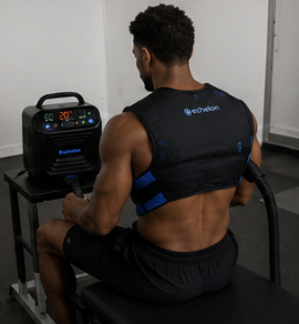 A man from behind wearing a black and blue Echelon cooling vest connected to a machine.