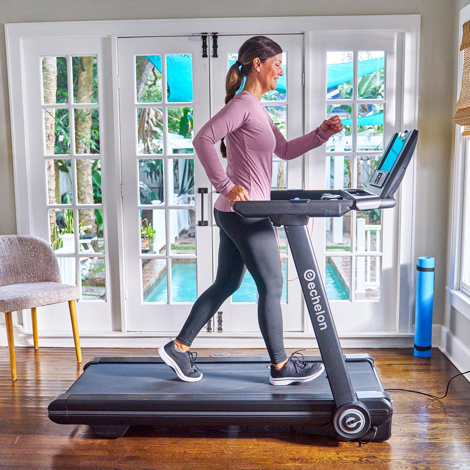Person walking on a treadmill indoors near large windows.