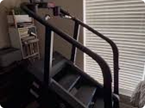 Stair stepper machine in a room with a bookshelf and blinds.